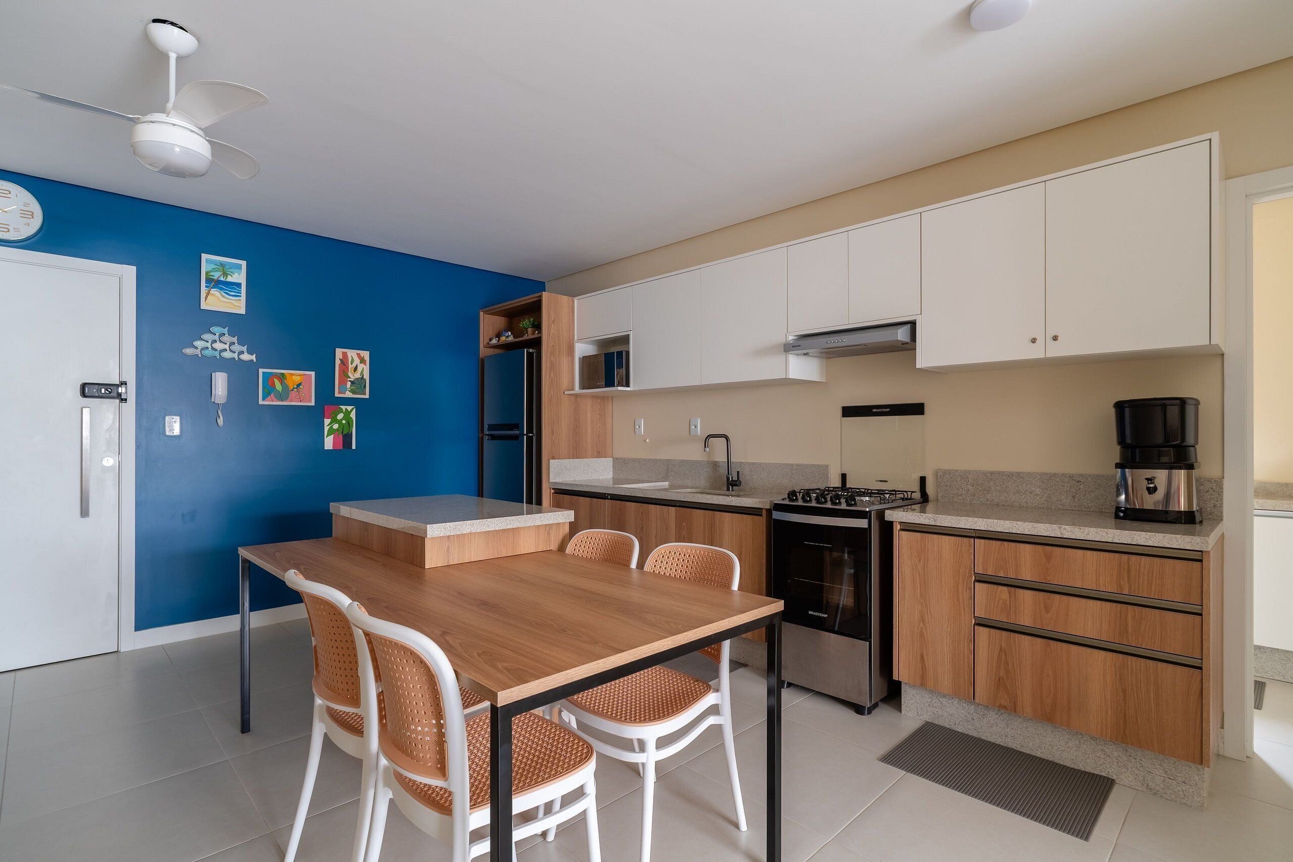 A modern kitchen with white cabinets, a wooden dining table, and a ceiling fan.