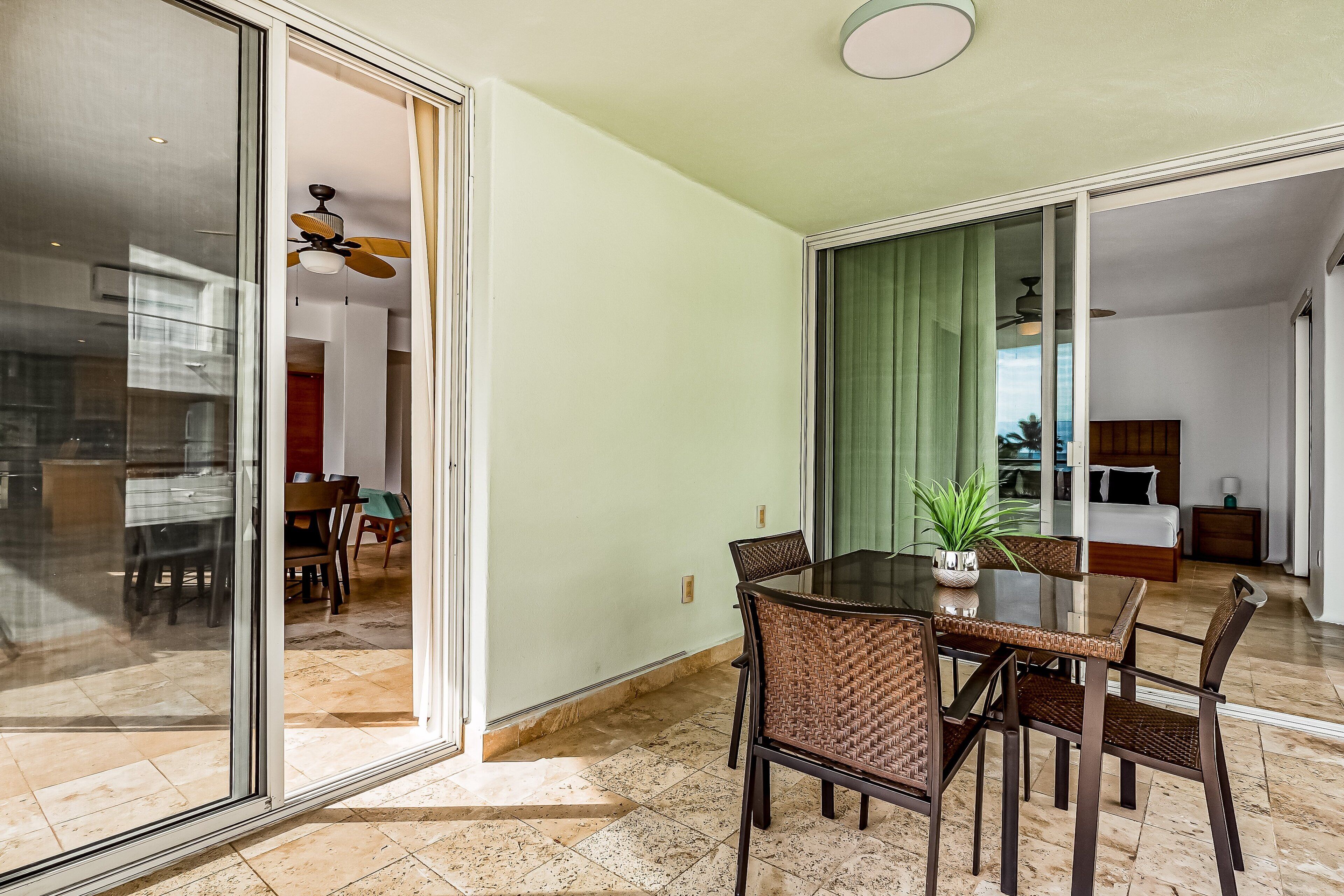 A dining area with a glass partition, wicker chairs, and a table with a potted plant.