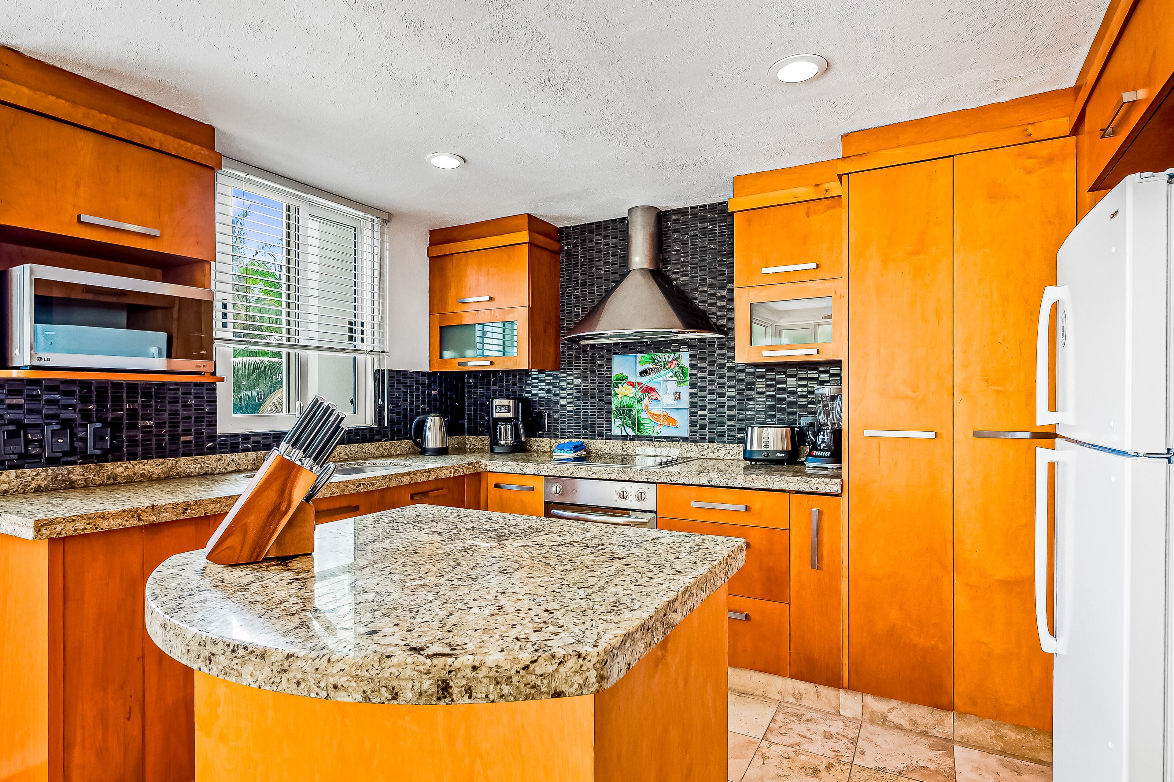 Una cocina con armarios de madera, encimera de granito, campana extractora de acero inoxidable y refrigerador blanco.