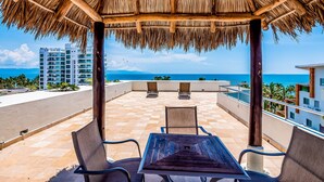 A covered outdoor seating area with a view of the ocean and buildings in the background. - Spacious Condo With Near the Beach With Resort-style Pool, Inviting Balcony (Nuevo Nayarit)