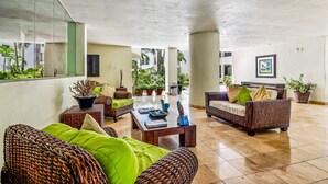 A spacious lobby with wicker furniture, a coffee table, and potted plants. - Spacious Condo With Near the Beach With Resort-style Pool, Inviting Balcony (Nuevo Nayarit)