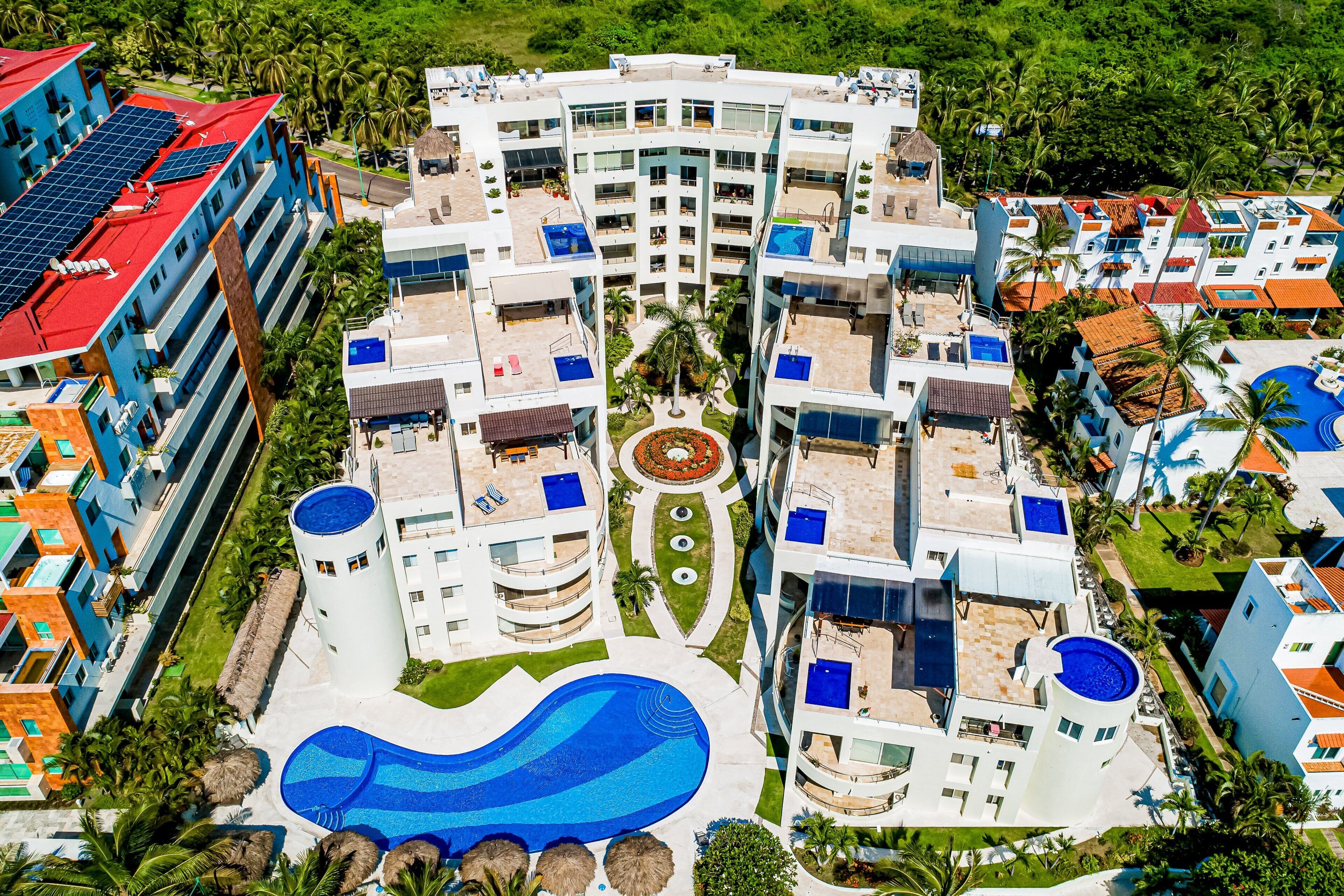 A multi-story hotel with a central swimming pool, balconies, and surrounding greenery.