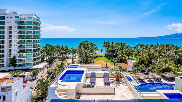 A resort with a pool area, palm trees, and a view of the ocean. - Spacious Condo With Near the Beach With Resort-style Pool, Inviting Balcony (Nuevo Nayarit)