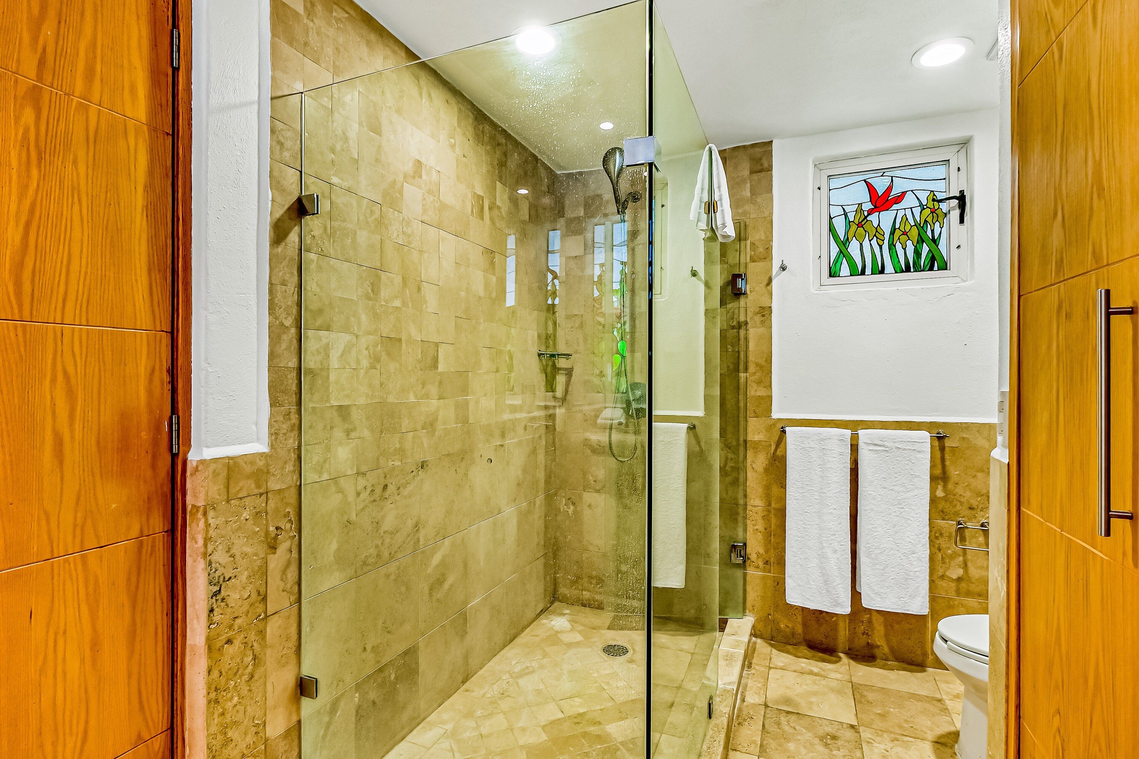 Une salle de bain moderne avec une douche à parois de verre, des toilettes blanches et une fenêtre décorative ornée de motifs floraux.