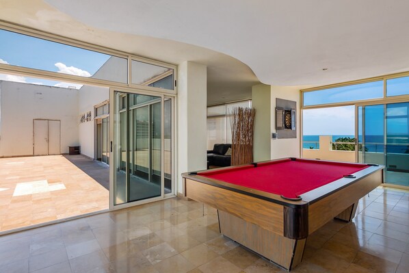 A pool table in a spacious room with large windows and a view of the sea. - Nitta Condo # 103 Stylish Condo Near the Beach With Ocean Views, On-site Pool (Nuevo Nayarit)