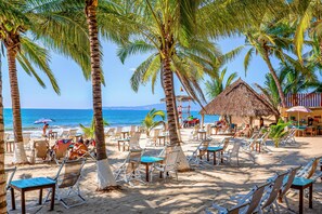 A beach with palm trees, lounge chairs, and a thatched-roof hut. - Nitta Condo # 103 Stylish Condo Near the Beach With Ocean Views, On-site Pool (Nuevo Nayarit)