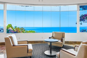Une pièce dotée d’une grande baie vitrée panoramique, de deux fauteuils, d’une petite table ronde et d’un tapis à motifs.