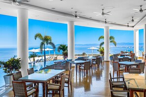 Un vaste espace extérieur aménagé pour les repas, avec des tables et des chaises, une piscine et une vue sur l’océan.