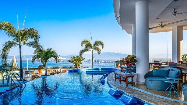 A pool with a view of the city, palm trees, and a seating area with tables and chairs. - Stylish Hillside Suite W/rooftop Pool, gym Access, AC & Family-friendly Layout (Puerto Vallarta)