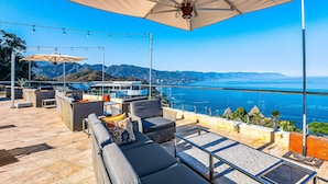 A rooftop terrace with outdoor seating, a large umbrella, and a view of the ocean. - Stylish Hillside Suite W/rooftop Pool, gym Access, AC & Family-friendly Layout (Puerto Vallarta)