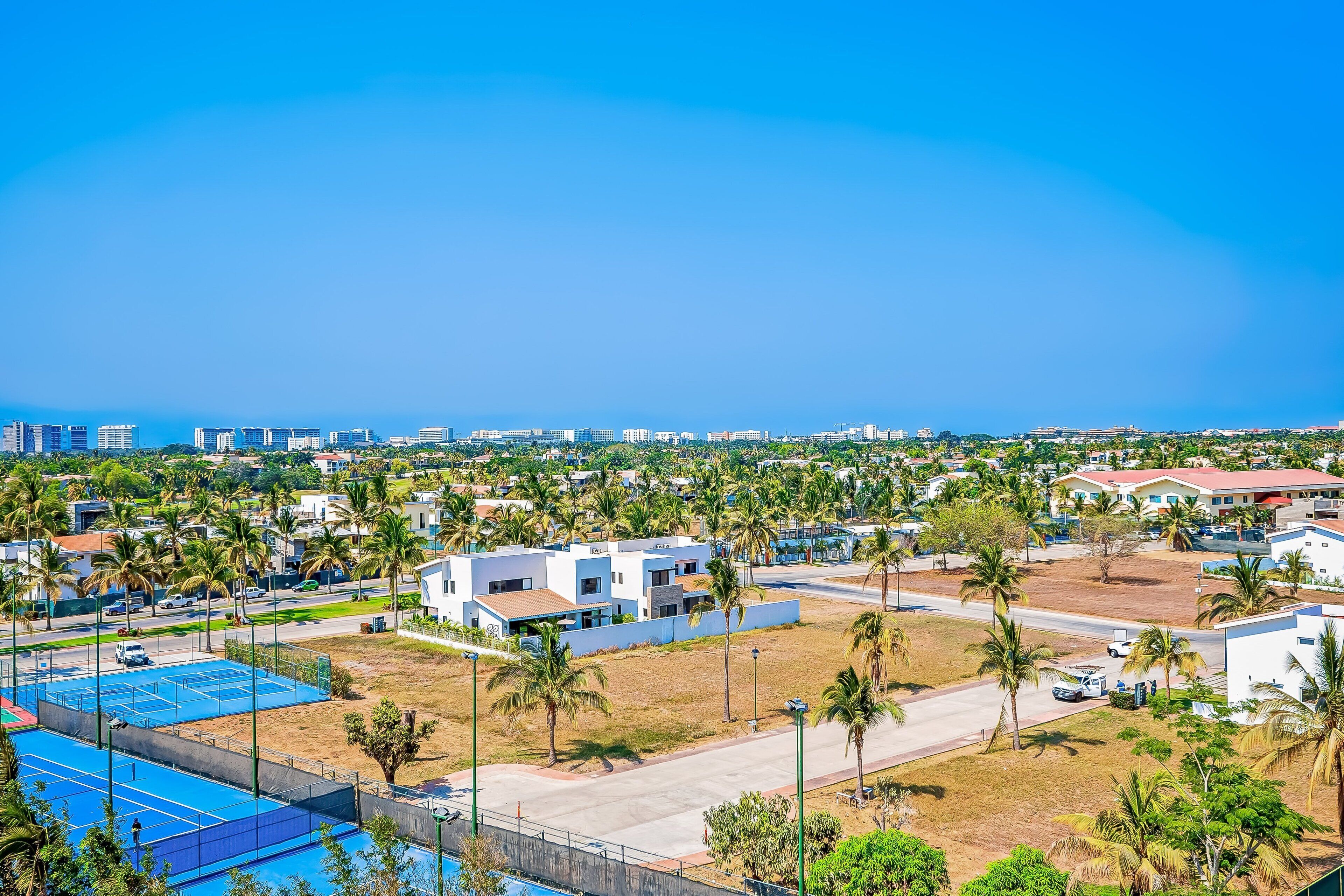 A residential area with modern buildings, a tennis court, and palm trees.