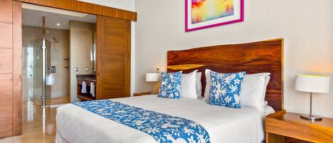 A hotel room with a large bed, wooden headboard, a glass shower, and a painting on the wall.