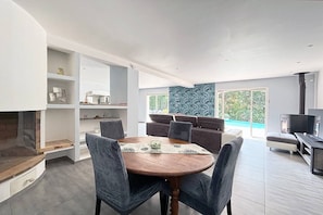 A modern living room with a fireplace, a dining area with a round table, and a large window with a view of greenery. - VILLA ST RAPHAEL 7 persons, walking distance to the beach, infinity pool (Saint-Raphaël)