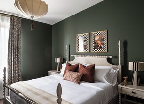 A bedroom with a bed, nightstands, a lamp, a wall-mounted light fixture, and two framed pictures.