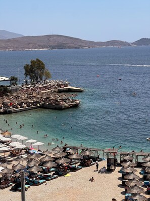 A beach with sun loungers and umbrellas, a pier with boats, and clear blue water. - FAMILY INN Apartments (Sarande)