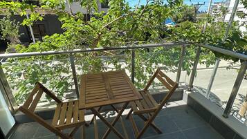 Ein Balkon mit Holztisch und Stühlen, umgeben von Grünpflanzen und einem wolkenlosen, blauen Himmel.