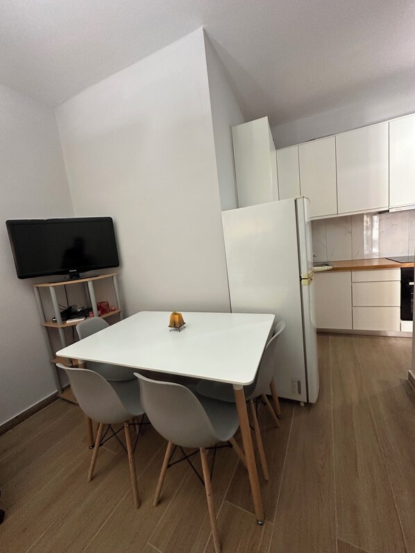 Une cuisine de taille réduite avec des meubles blancs, une table blanche et deux chaises.