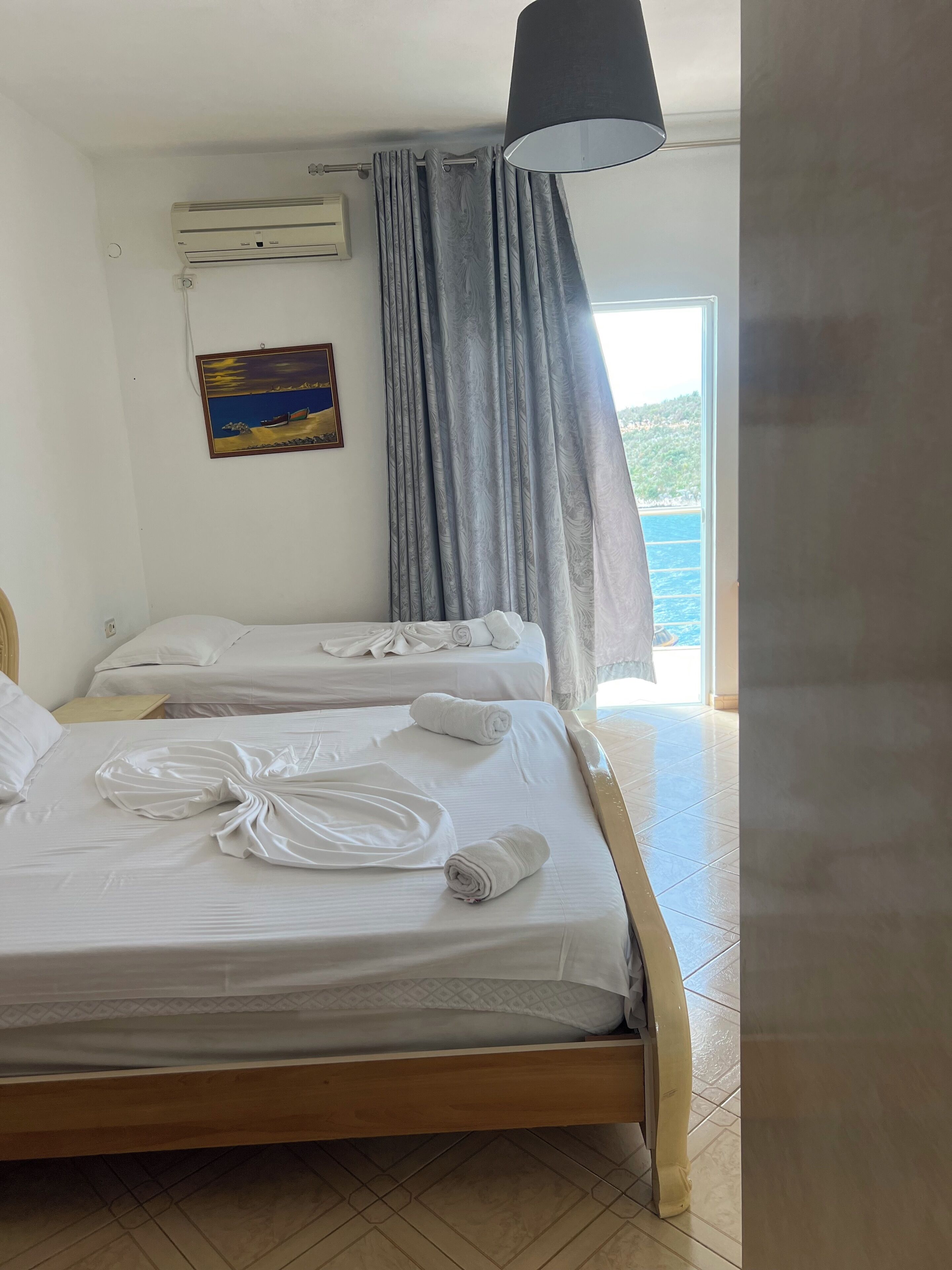 A hotel room with two beds, a painting on the wall, a window with curtains, and a ceiling lamp.
