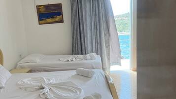 A hotel room with two beds, a painting on the wall, a window with curtains, and a ceiling lamp.