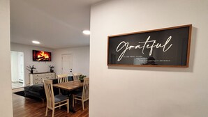 En matplats med ett träbord och stolar, en tv som är monterad på väggen och en inramad, inspirerande citat.