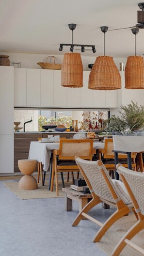 Une cuisine moderne avec des meubles blancs, un coin repas doté de chaises en osier et des luminaires suspendus.