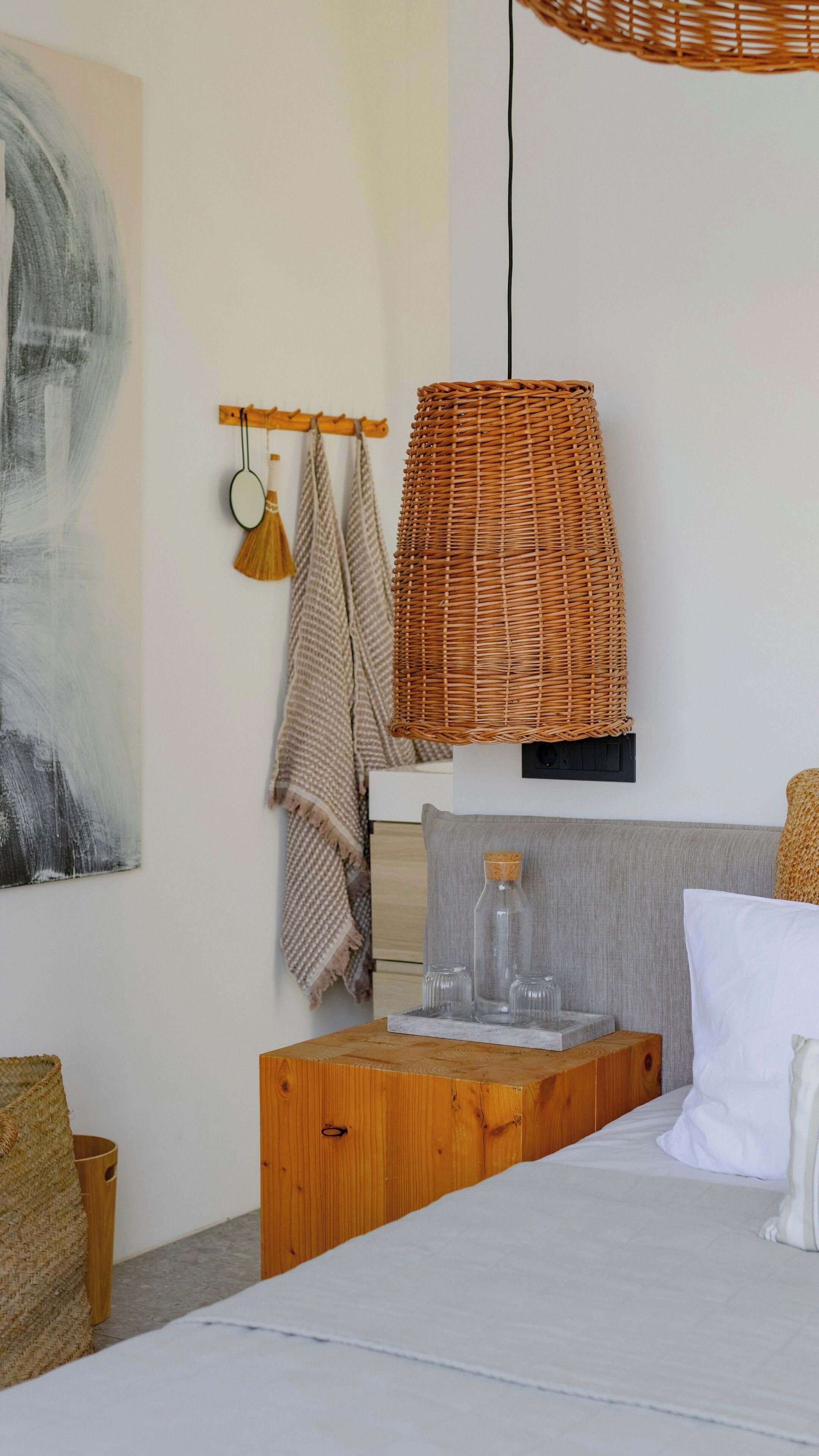 A bedroom with a bed, a wooden nightstand, a wicker lamp, and a wall-mounted shelf with glass jars.