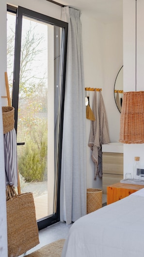 Ein Schlafzimmer mit einem großen Schiebeglasfenster, einem Bett, einem Nachttisch aus Holz und einem Korbwäschekorb.