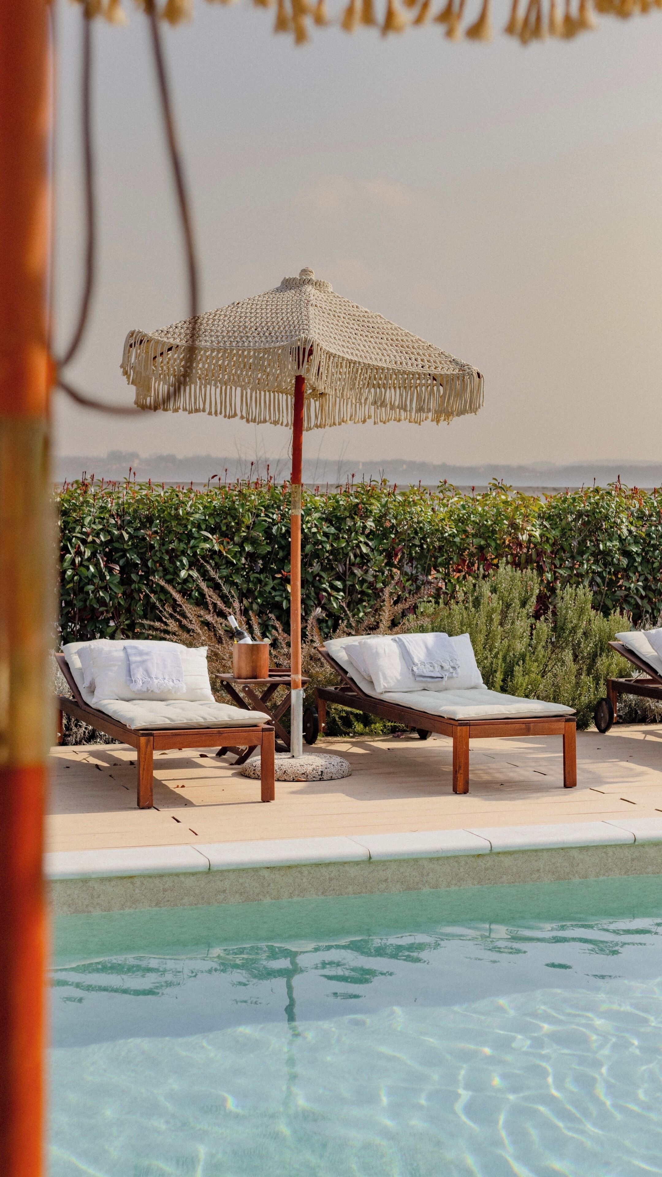 A poolside area with two lounge chairs, a woven umbrella, and a view of the landscape.