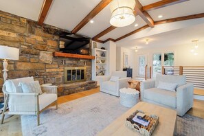 Un salón acogedor con chimenea de piedra, sofás blancos y techo de madera.