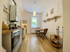 A compact kitchen with modern appliances, a dining area with a wooden table and chairs, and a view through a window. - Cozy vacation apartment in a good location (Görlitz)