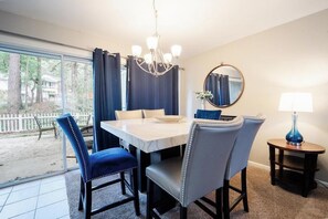 Un espace repas comprenant une table, des chaises, un lustre, un miroir rond et une lampe.