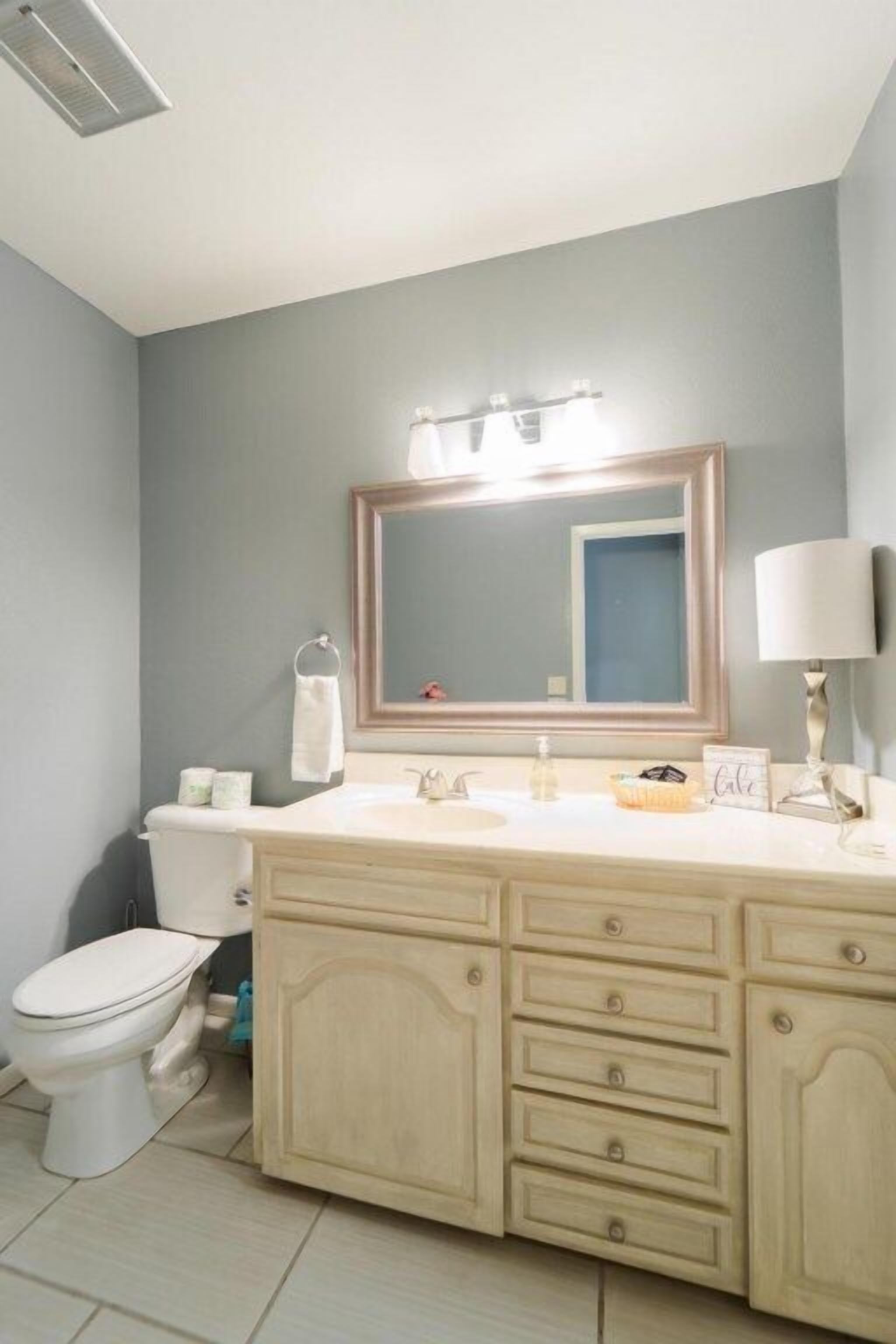 A bathroom with a toilet, a sink with a mirror, and a vanity with drawers.