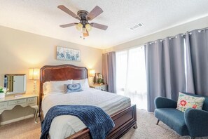 A hotel room with a bed, a desk, a chair, a ceiling fan, and a window with curtains.