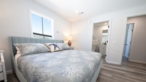 Ein Schlafzimmer mit einem Bett, Nachttischen, einem Fenster und einer Tür zu einem anderen Raum.