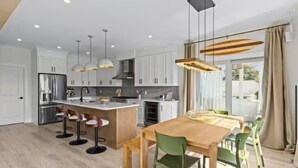 Et moderne køkken med en central ø, hængende lamper og et spiseområde med stole.