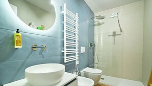 Een moderne badkamer met een groot wit wastafel, toilet, douche en handdoekhouder.