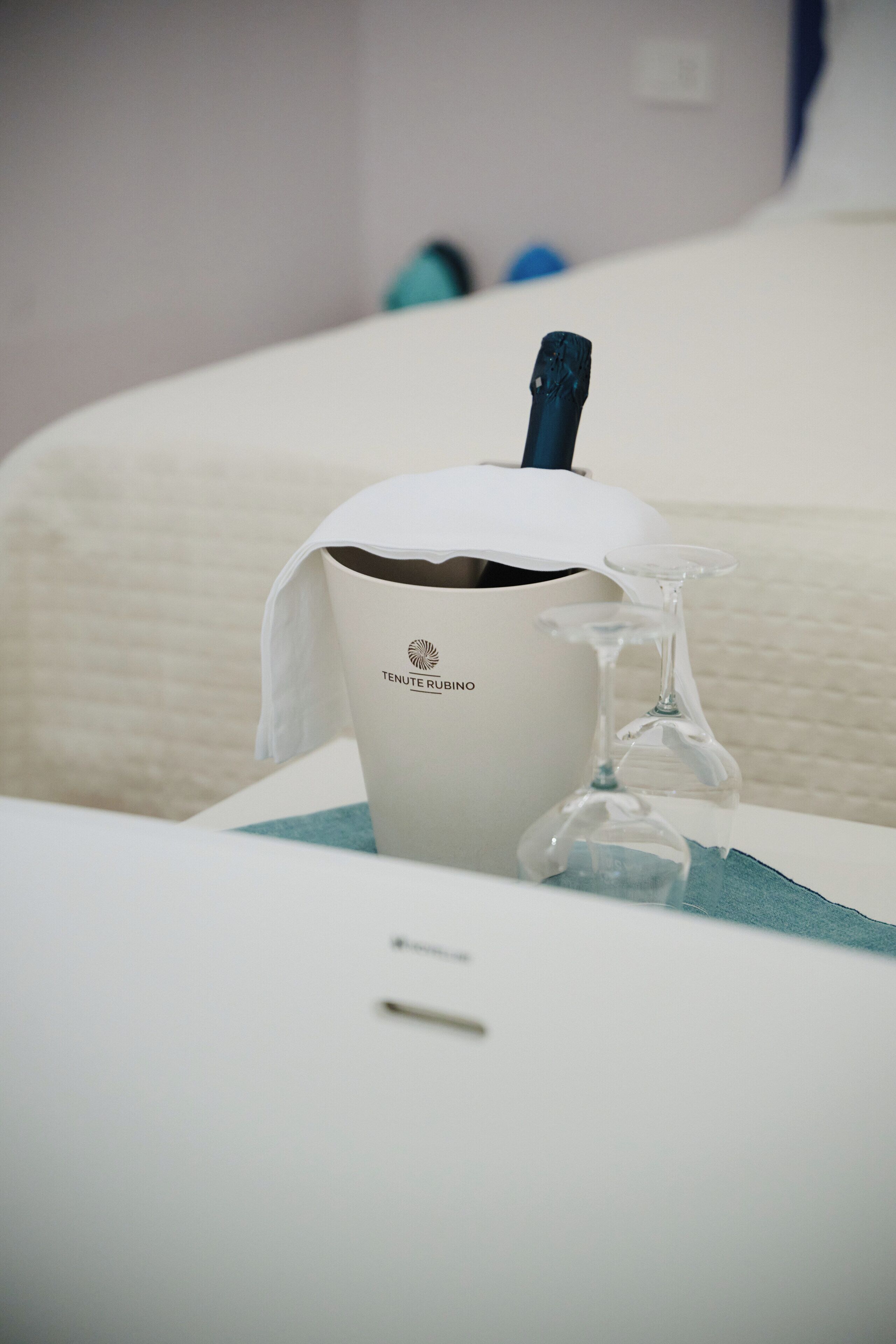 Una taza blanca con la etiqueta 'TENUTE RUEBINO' y un objeto de vidrio transparente sobre una mesa.