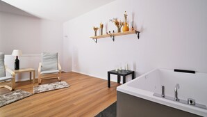 Een moderne badkamer met een bad, een houten vloer, een klein tafeltje met kaarsen en een plank met decoratieve voorwerpen.