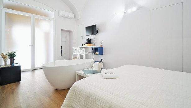 Een moderne hotelkamer met een groot bed, een badkuip, een klein tafeltje en een aan de muur bevestigde televisie.