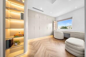Une pièce moderne dotée d’une grande fenêtre, de bibliothèques intégrées, d’un parquet en bois disposé en chevrons et d’un espace bureau.