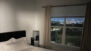 Une chambre d’hôtel avec un grand lit, une table de chevet, un miroir et une fenêtre donnant sur la ville.