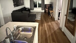 Une cuisine moderne avec un évier en acier inoxydable, un coin repas comprenant une table et des chaises, un canapé et une grande fenêtre avec des rideaux.