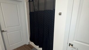 Un couloir avec un plancher en bois, une porte blanche, un rideau noir et un tapis gris.