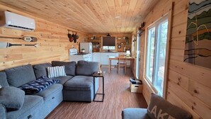 Ein Interieur einer Holzhütte mit Holzbalkendecke, einer Couch, einem Esstisch und einer Küchenzeile.