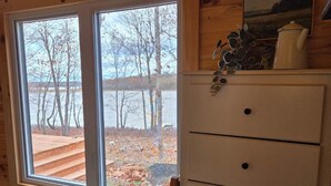 Ein Blockhauszimmer mit großem Fenster, Holzwänden, einem weißen Schminktisch und einem Bett mit gemustertem Überwurf.