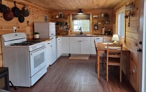Una cocina compacta con gabinetes blancos, una estufa a gas, un refrigerador y un comedor con mesa y sillas.