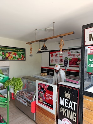 Interior de una carnicería con una vitrina de carne, una balanza y un cartel que anuncia entrega de carne fresca.