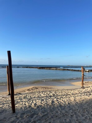 Ein Sandstrand mit einem hölzernen Pfosten und Seilabsperrung, ruhigem Meer und blauem Himmel.
