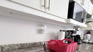 Une cuisine dotée d’un évier en acier inoxydable, d’un plan de travail en granit, de meubles blancs et d’un égouttoir à vaisselle rouge.