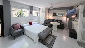Une chambre moderne avec un lit, des tables de chevet, un canapé, une petite table ronde et un téléviseur.